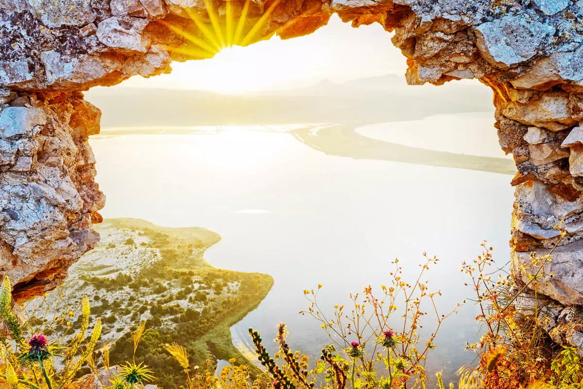 Explore Messinia-Header-The amber light of sunrise spills over Navarino Bay, framed by the ancient stone window of a forgotten ruin.
